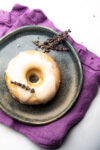 A vegan lemon cake donut with lavender icing on a plate.