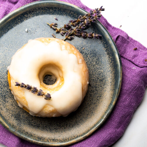 A vegan lemon cake donut with lavender icing on a plate.