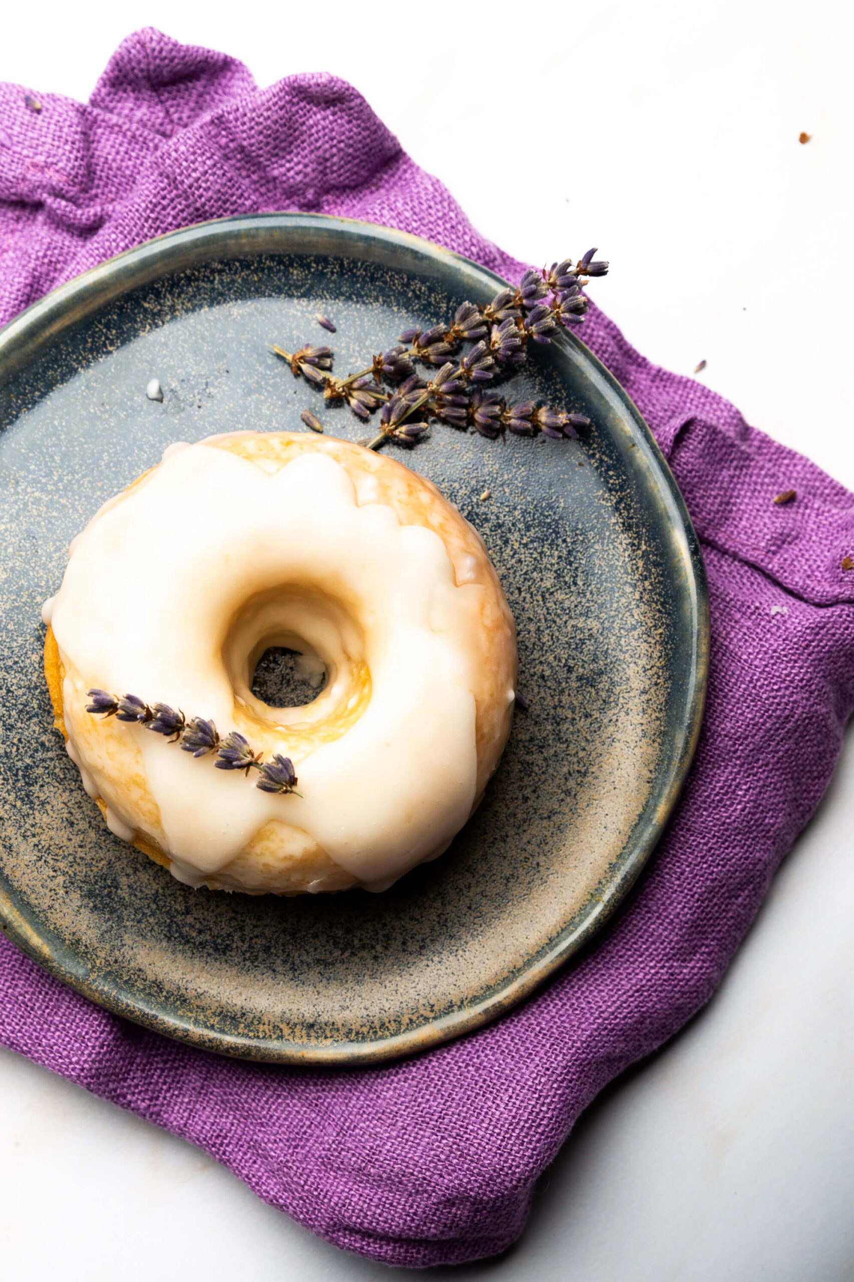A vegan donut with lavender icing on a plate.