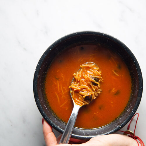 A person holding a bowl of soup with a spoon, enjoying a warm serving of Sopa de Fideo.