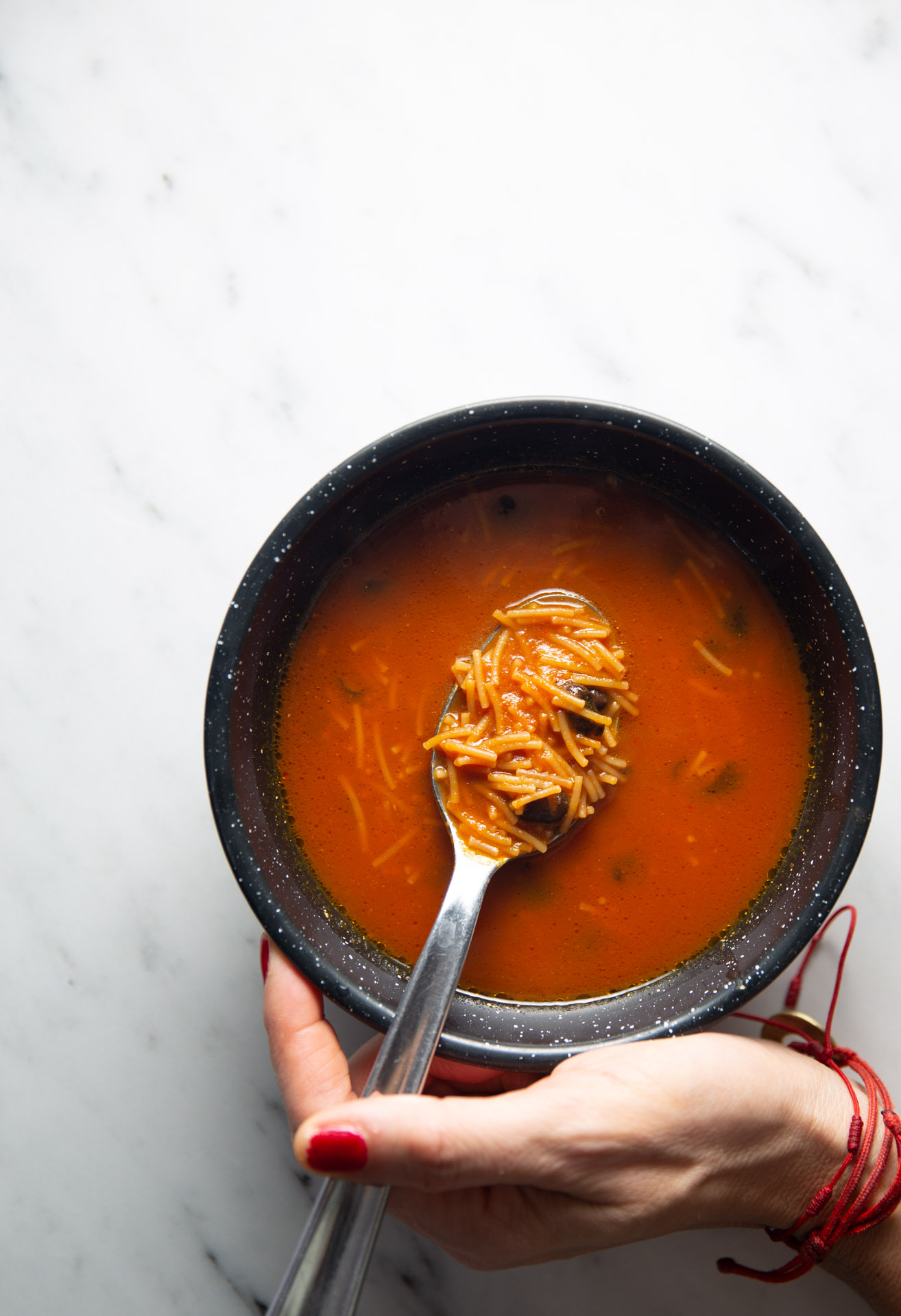 A person holding a bowl of soup with a spoon, enjoying a warm serving of Sopa de Fideo.