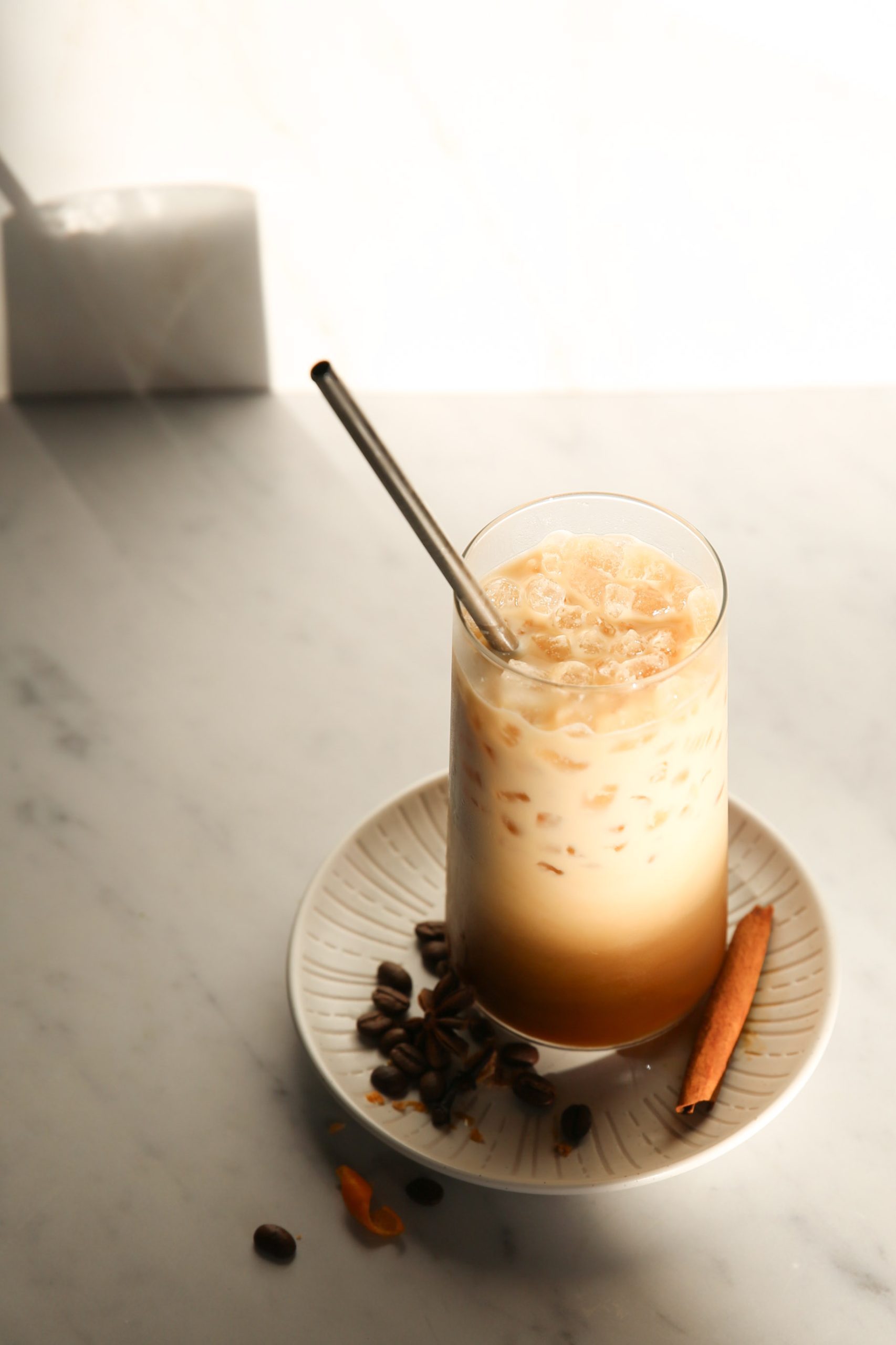 An iced café de olla with cinnamon and coffee beans on a plate.