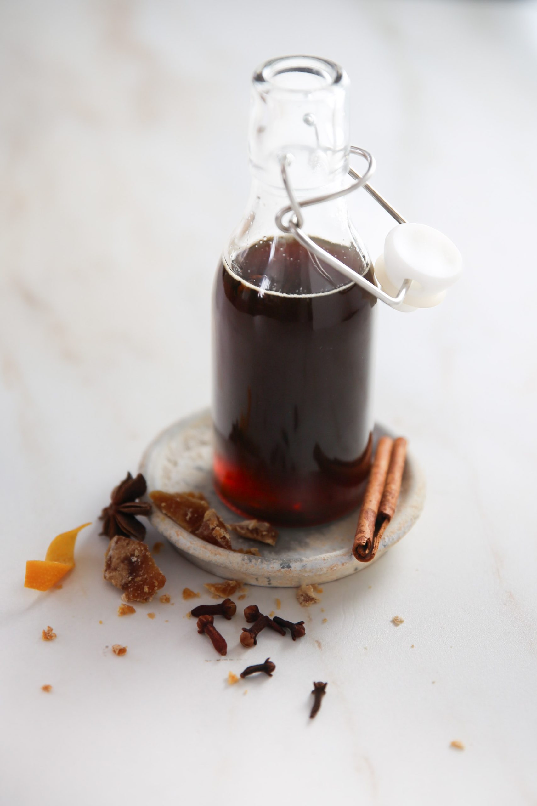 A glass bottle with cinnamon sticks and spices on a white plate, accompanied by Cafe de olla syrup.
