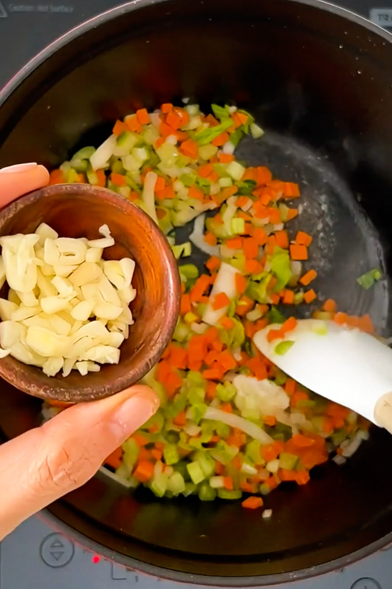 A person is stirring some chopped vegetables in a pan, preparing a vegan soup.
