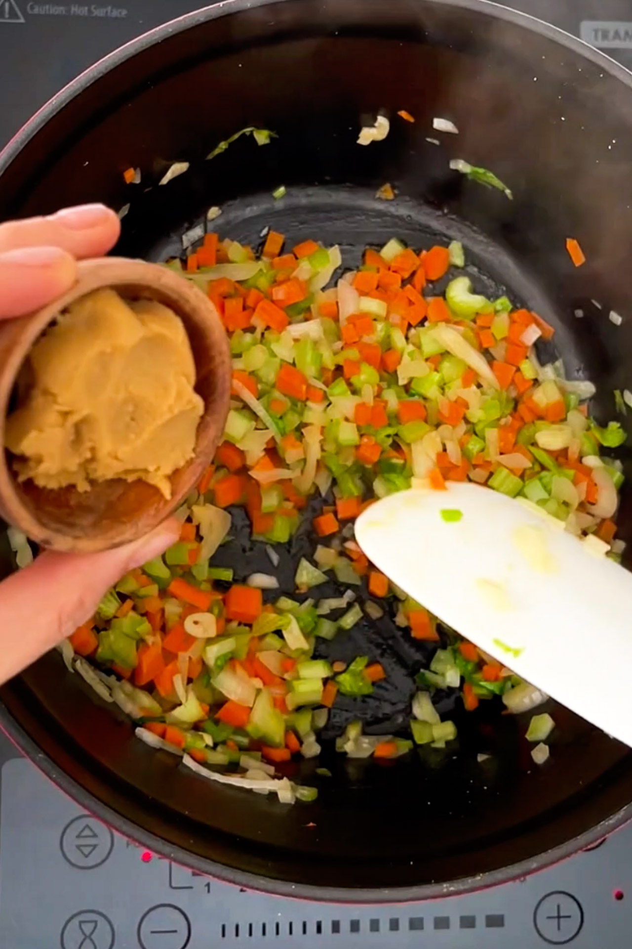 A vegan stirs vegetables in a pan with a spoon to prepare a noodle soup.