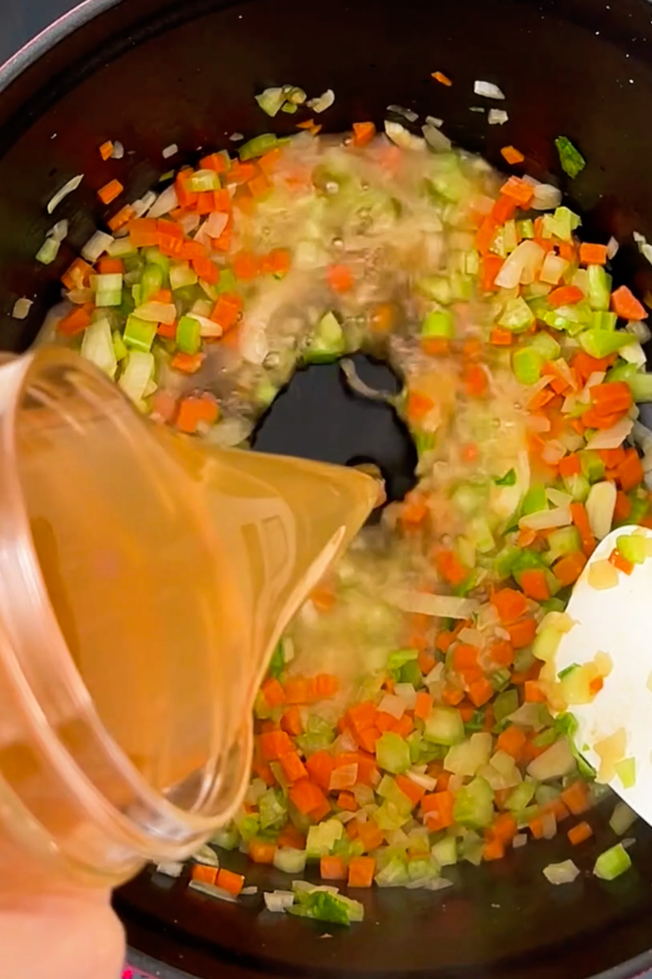 A person is pouring sauce into a pot of vegan soup.
