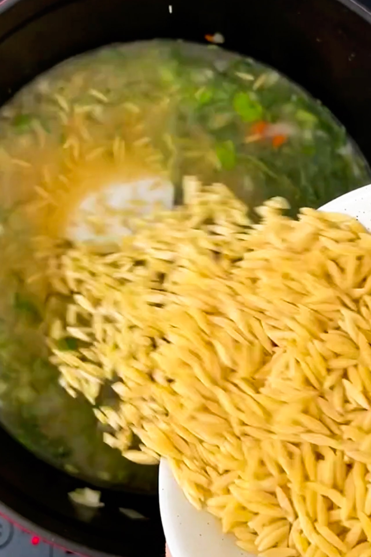 A vegan is pouring noodles into a pot of soup.