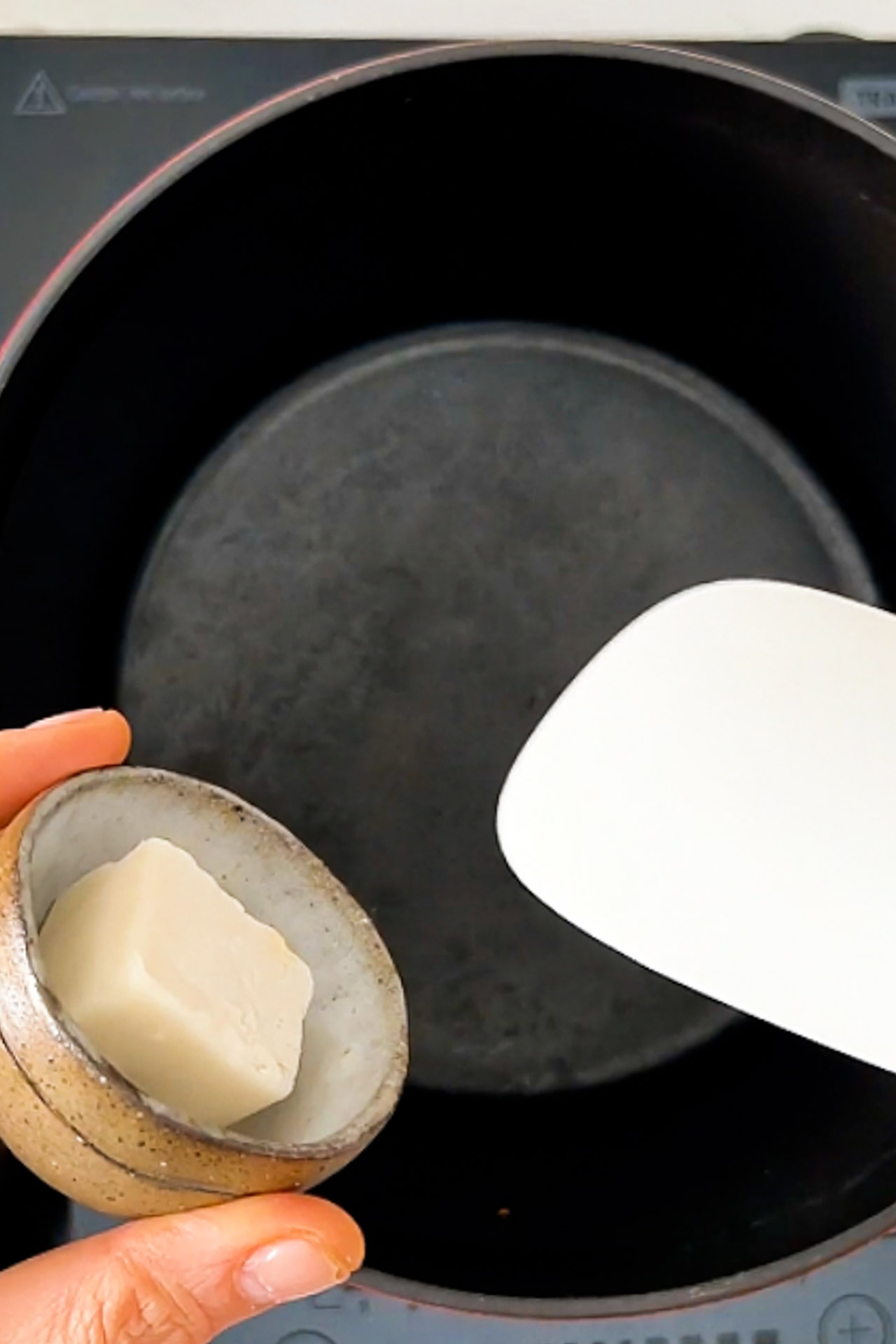 A person is holding a piece of butter in a vegan soup pan.