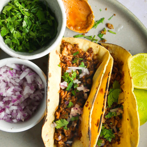 Two tacos on a plate with limes.