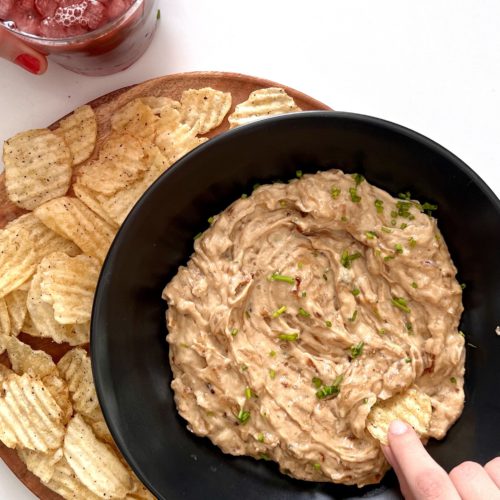A person is dipping a plate of vegan salsa into a plate of salsa.
