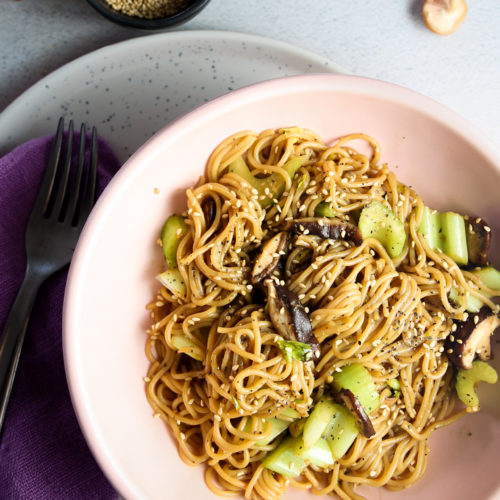 A bowl of noodles with mushrooms and black pepper sprinkled with sesame seeds.