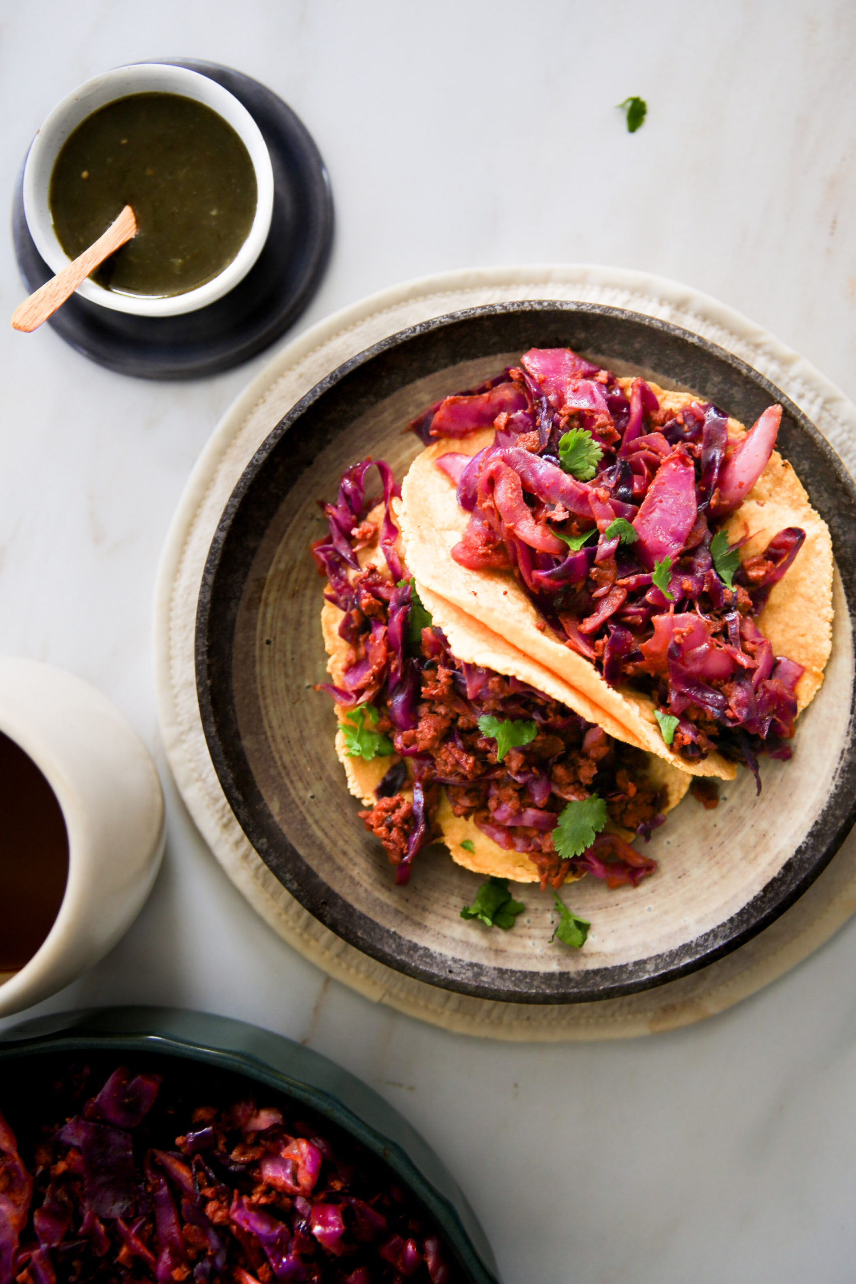 red cabagge chorizo tacos on a grewy plate with a small bowl of salsa on the side.