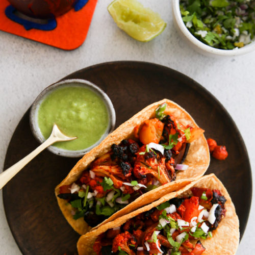 Two tacos on a plate next to a plate of guacamole.