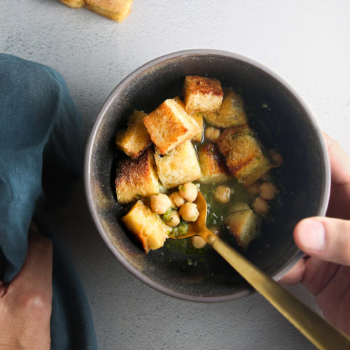 Croutons in a bowl with a person holding a spoon for Portuguese Soup.