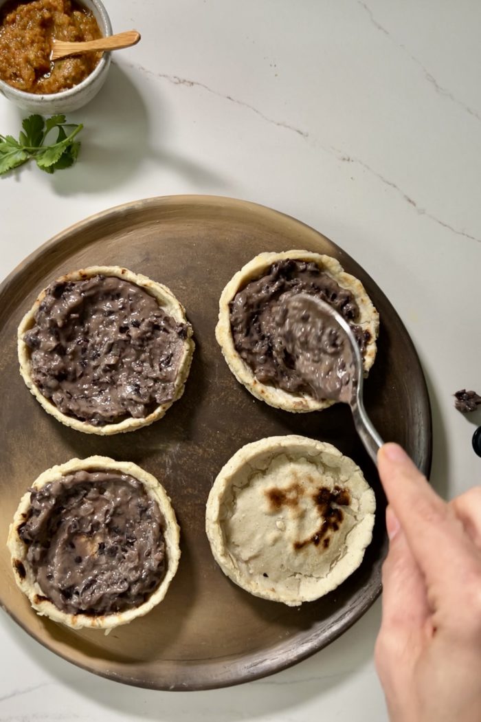 Untando frijoles refritos sobre un sope casero como base del relleno.
