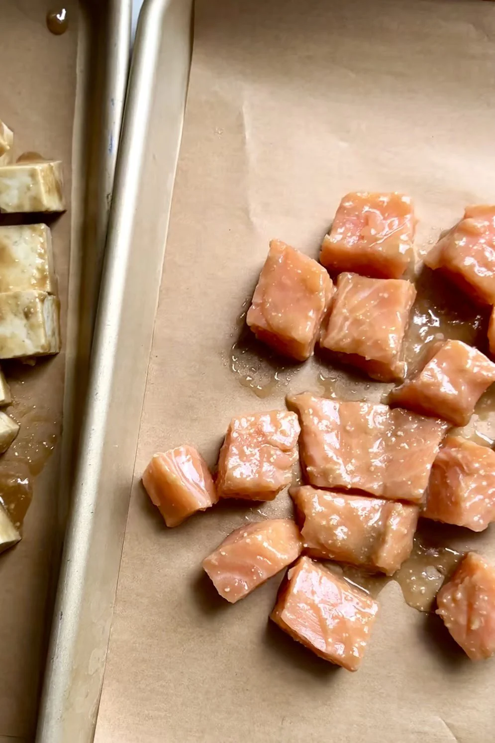 Cubed raw salmon and tofu are placed on parchment paper, ready for a delicious miso salmon bowl. The glossy pinkish-orange salmon contrasts with the marinated tan tofu, each arranged separately for this vibrant miso salmon recipe.