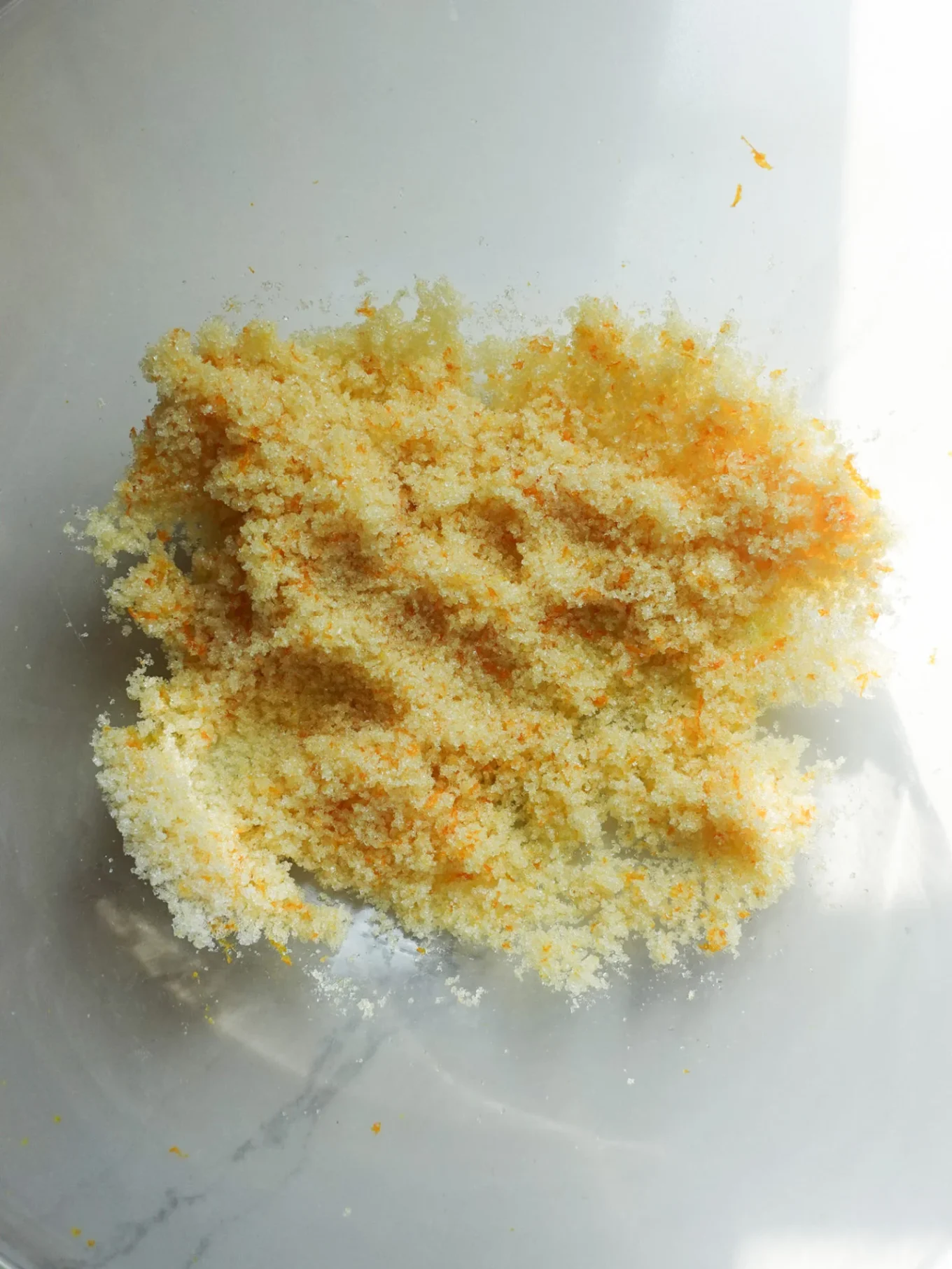 A close-up of a mound of granulated sugar mixed with finely grated orange zest on a white surface, evoking the vibrant look of Authentic pan de muerto, a traditional Mexican bread enjoyed during the Day of the Dead.