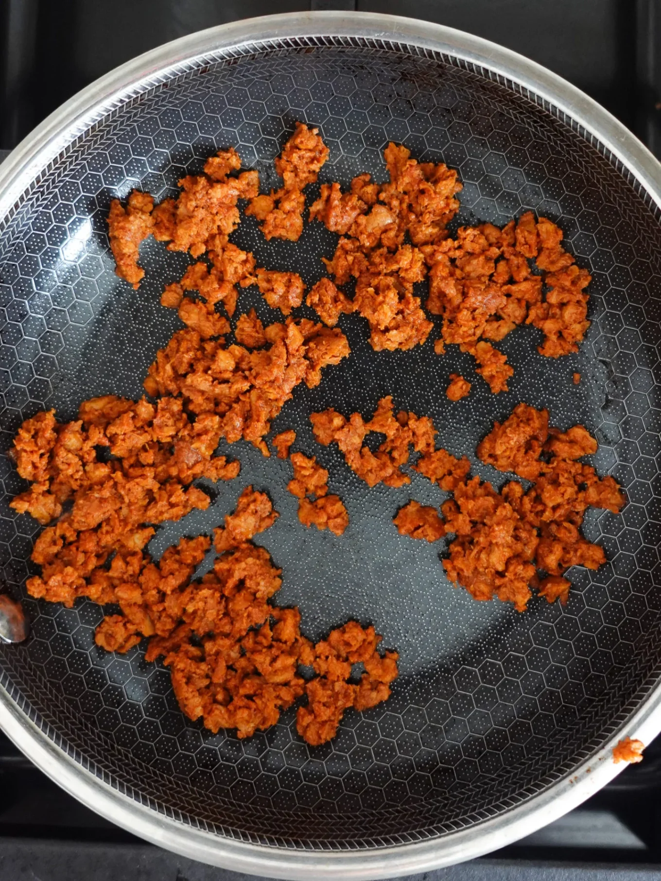 Cooked ground spiced meat, browned and crumbly—likely Mexican chorizo—spreads unevenly in a nonstick skillet with a hexagonal pattern. The pan sits on a stove, and the filling looks perfect for tacos or a torta de chorizo.