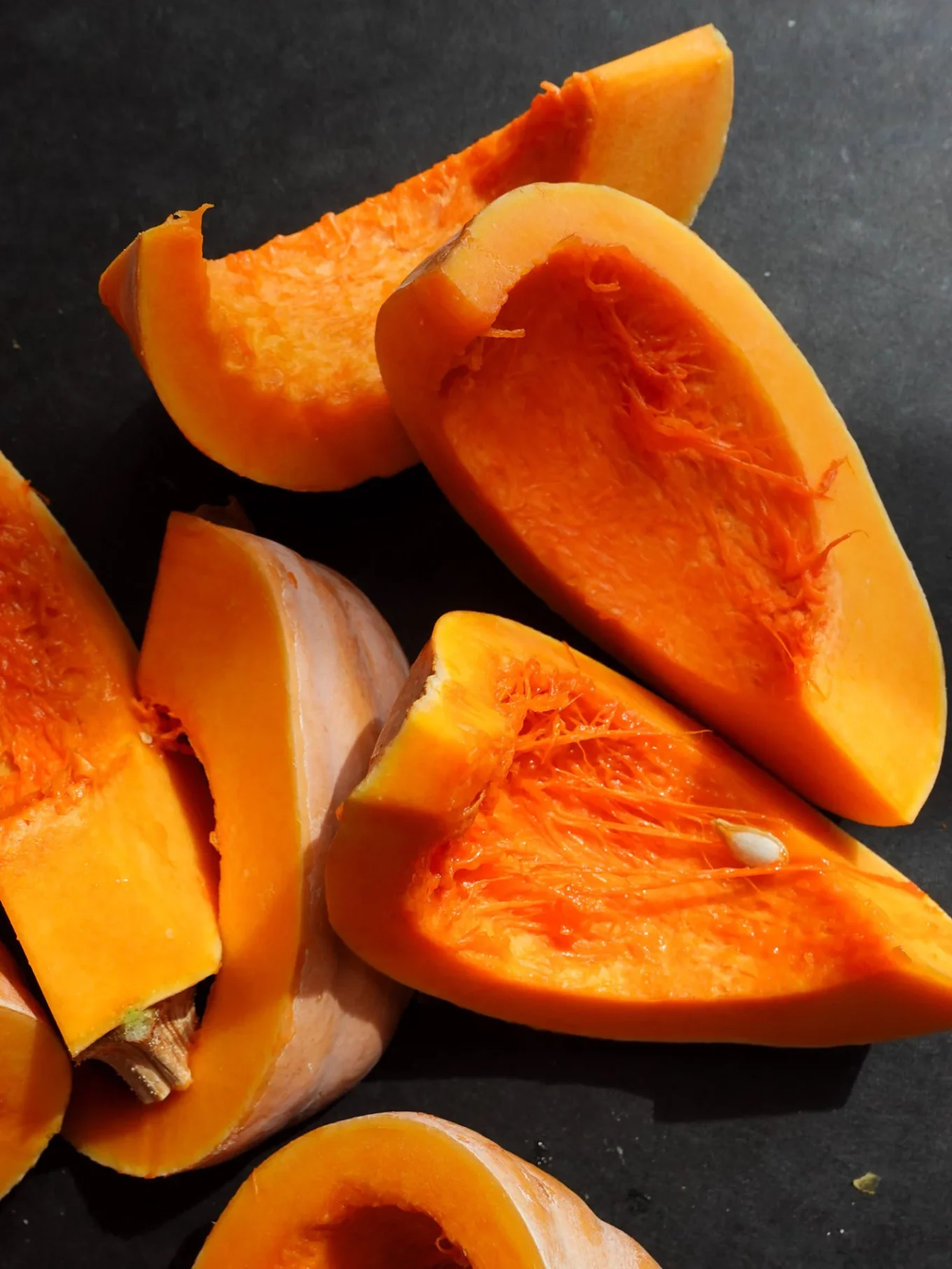 Close-up of several pieces of raw butternut squash, similar to what’s used in Calabaza en Tacha, a Mexican pumpkin dessert. The large chunks reveal bright orange flesh and fibrous interior, with pale beige skin contrasting the vibrant sweet pumpkin inside.