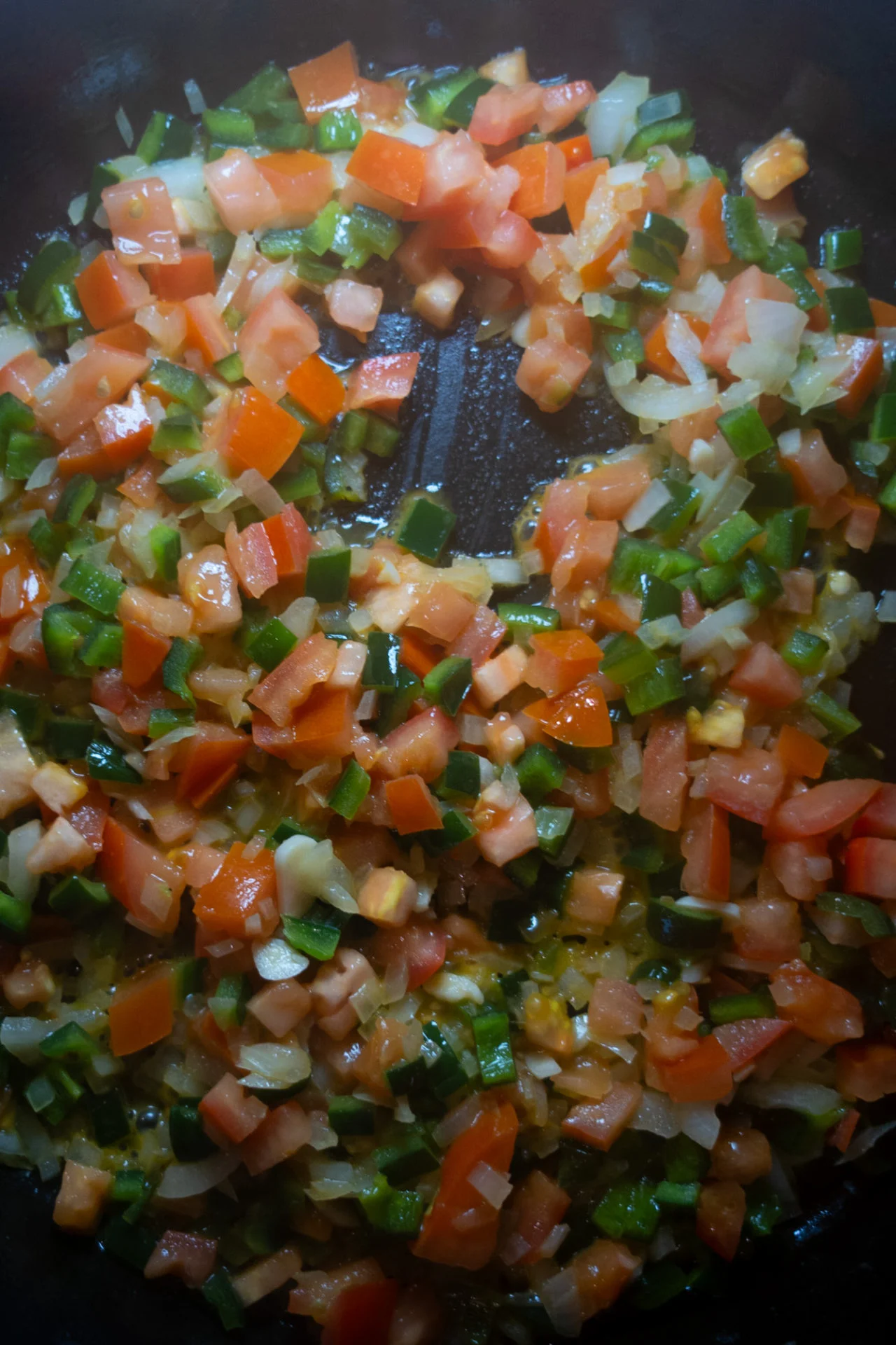 Diced tomatoes, onions, and green peppers are being sautéed in a pan. The vibrant, freshly chopped vegetables glisten with oil—perfect as a flavorful base for Shrimp Tacos or classic Mexican Tacos.