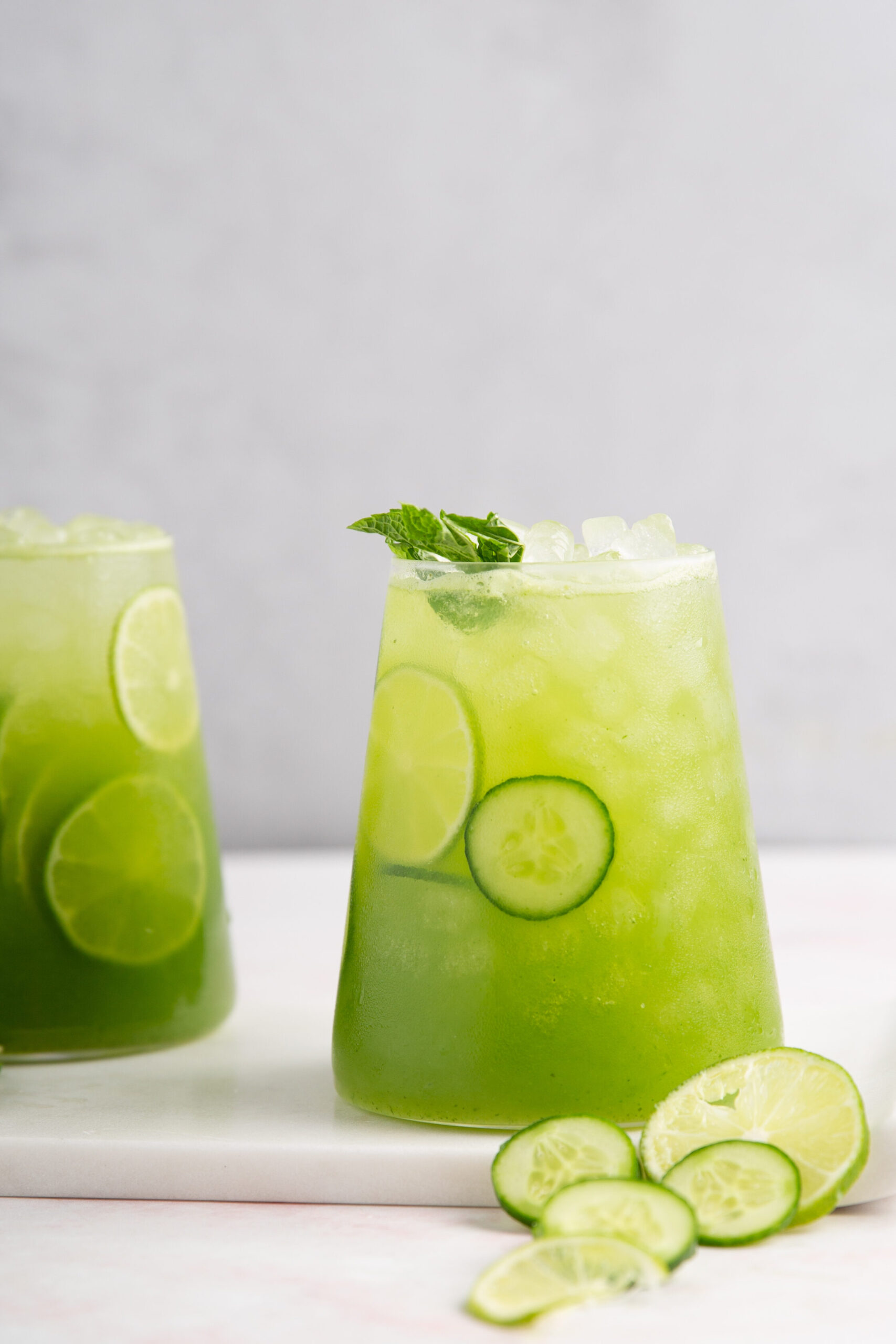 Two glasses of cucumber lime agua fresca with mint served with ice, lime slices, and fresh mint leaves