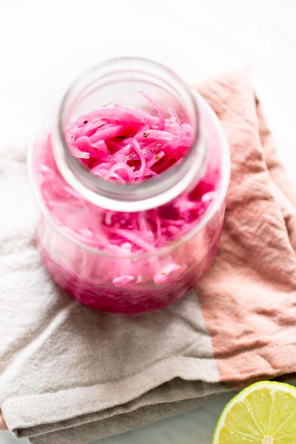 Jar of Mexican pickled red onions with a halved lime on a white surface